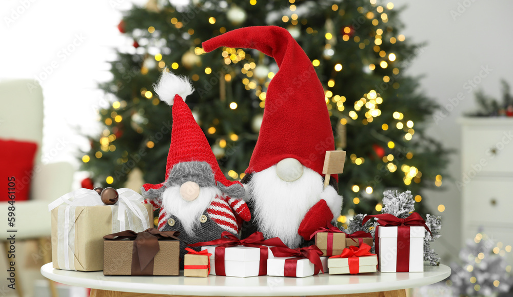 Fototapeta premium Funny Christmas gnomes and gift boxes on coffee table in room with festive decoration