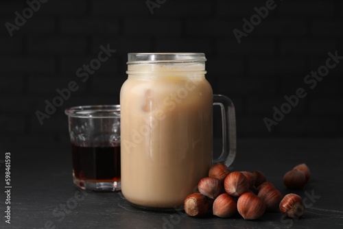 Mason jar of delicious iced coffee, syrup and hazelnuts on black table