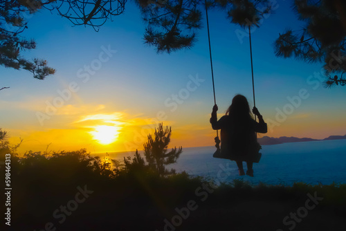 Silhouette of a girl swinging in the sunset