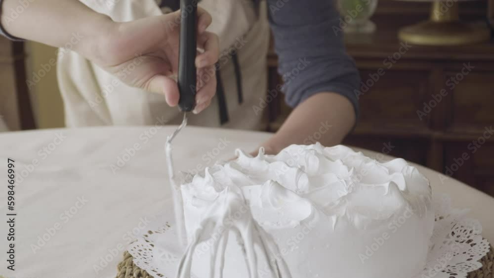 focus passes from the mixer nozzle to the hands of the pastry chef delicately finishing (with a spatula) cake with white meringue, close up focus passes from the mixer nozzle to the hands of the pastry chef delicately finishing (with a spatula) cake with white meringue, close up