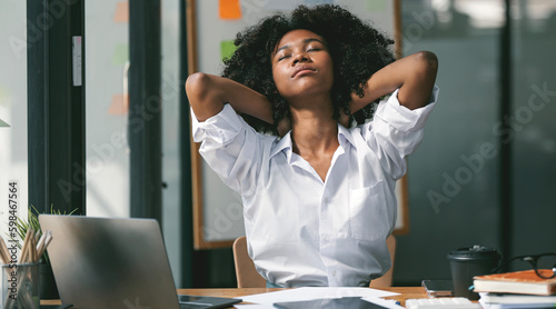 Stressed tired young Black freelance woman suffering from migraine, headache at workplace. photo