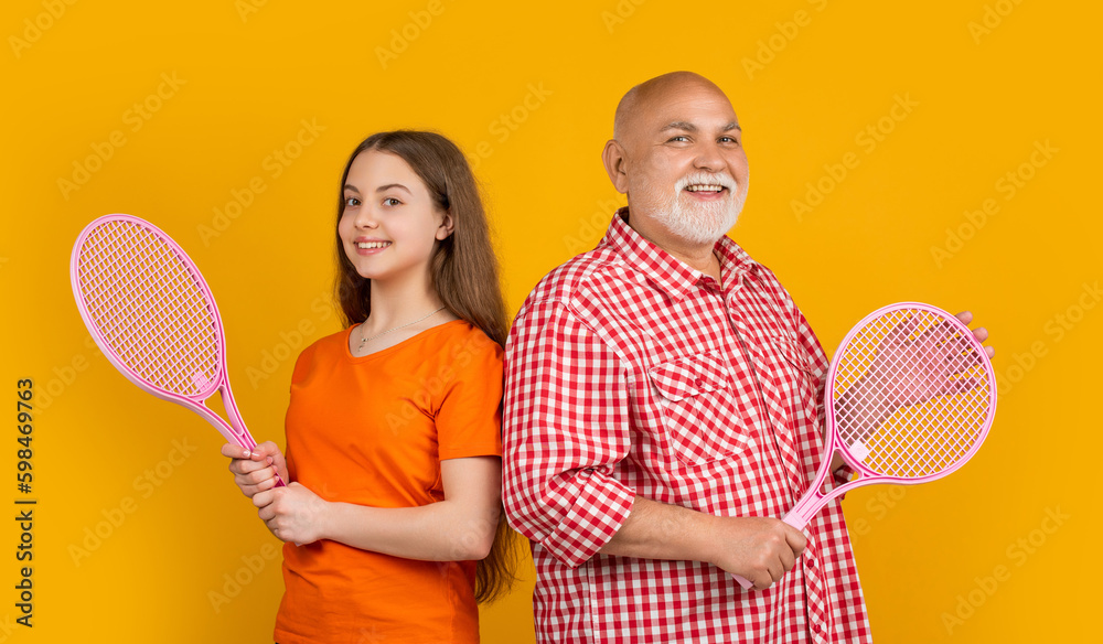 cheerful teen girl with grandfather with badminton racket on yellow background cheerful teen girl with grandfather with badminton racket on yellow background