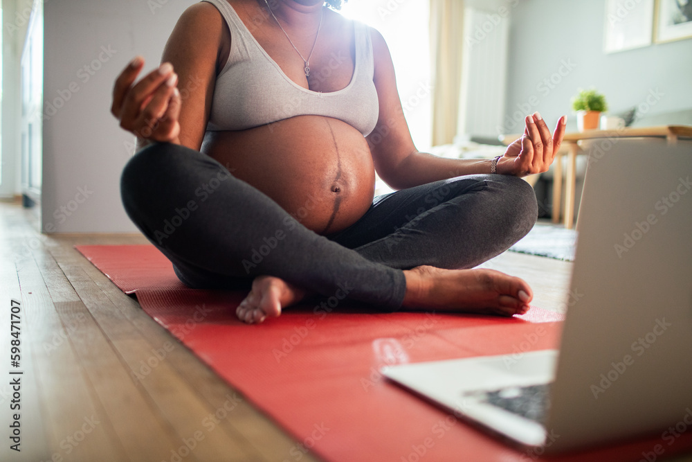 Fototapeta premium Young pregnant latina woman meditating at home wihle using a laptop
