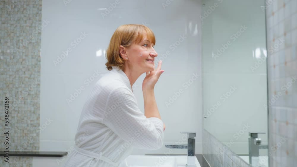 Caucasian senior woman looking at mirror then apply lotion on face. Caucasian senior woman looking at mirror then apply lotion on face.