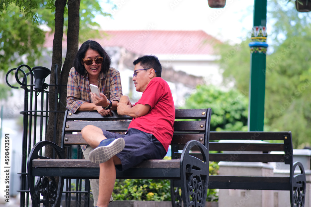 Fototapeta premium Couple of man and woman sitting on a park bench looking at their smartphone together