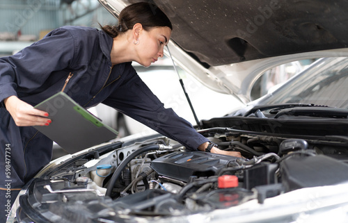 Female auto mechanic checking car engine to repair in mechanics garage. Engineer woman open vehicle hood to diagnose problems at engine room for maintenance or fix. Empowering woman in motor business.