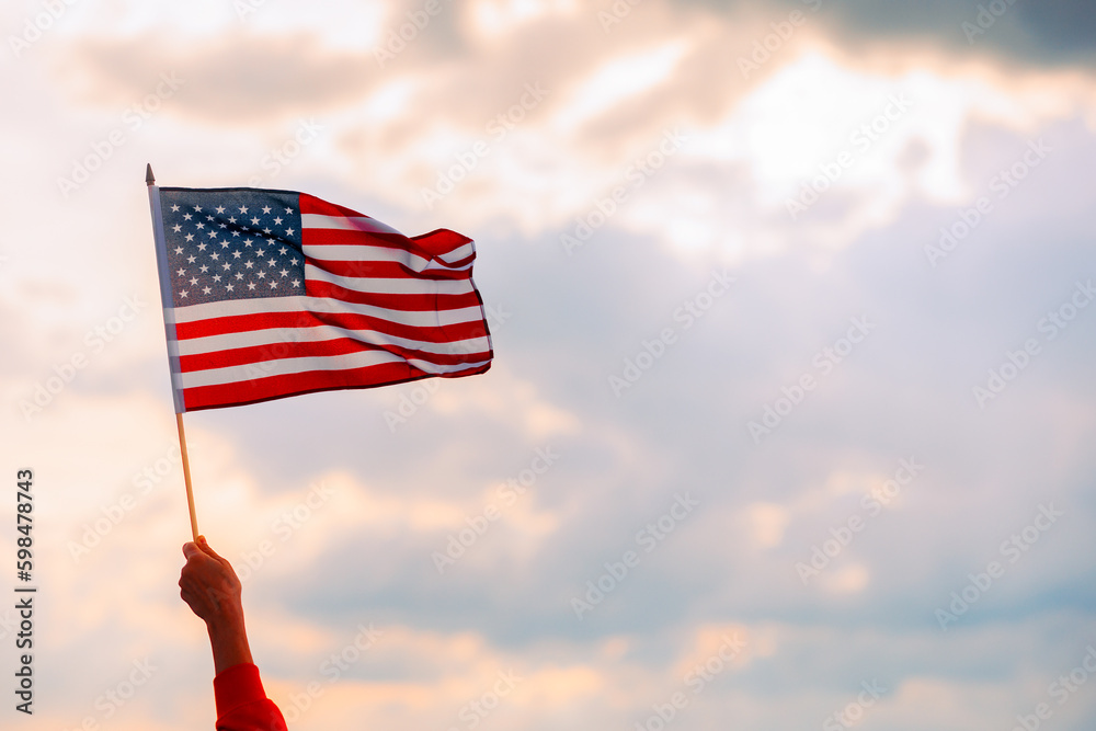 Hand Waving the Flag of the United Stated of America. Optimistic person holding American flag celebrating citizenship
 - obrazy, fototapety, plakaty 