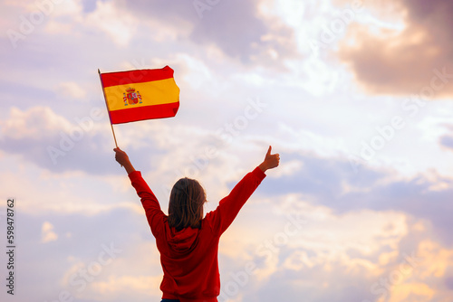 Woman Waving Spanish Flag Looking at the Sky. Optimistic girl holding national flag celebrating citizenship
 photo