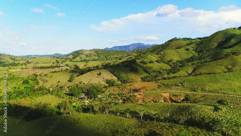 Summer in the Dominican mountains. Green grass and summer blue sky landscape. Scenic panoramic view of idyllic hills landscape with mountain peaks on a beautiful sunny day with blue sky and clouds. Summer in the Dominican mountains. Green grass and summer blue sky landscape. Scenic panoramic view of idyllic hills landscape with mountain peaks on a beautiful sunny day with blue sky and clouds.