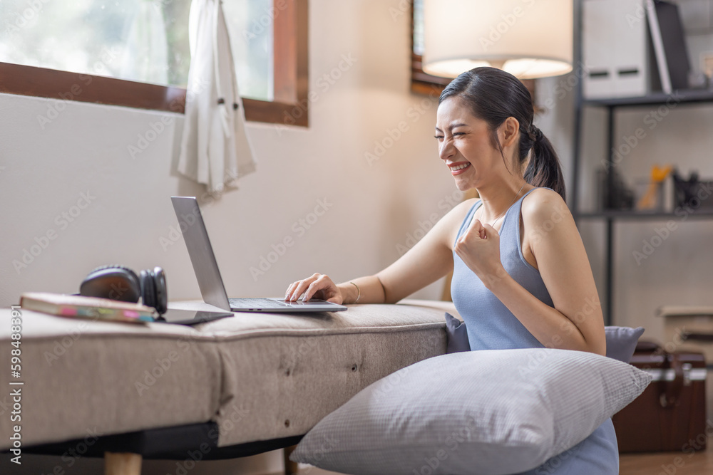 Obraz premium Beautiful Young Asian woman using laptop computer on sofa at home, shopping online with internet in happy mood and Relax part time concept