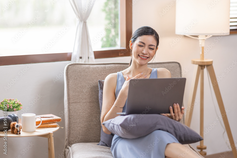 Portrait of a young happy asian female freelancer sitting on the couch and working on project, watching movie on laptop, studying, blogging, resting and chatting online. 