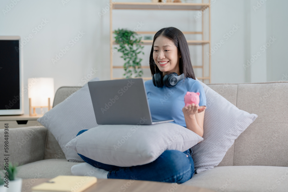 Asian young woman holding a piggy bank and using computer, Savings concepts. Asian young woman holding a piggy bank and using computer, Savings concepts.