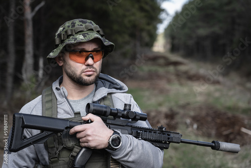 A soldier in goggles and a panama hat on his head with a rifle with an optical sight in his hands.