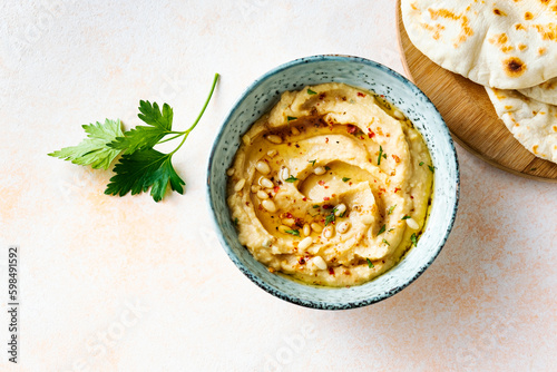 Homemade hummus with pine nuts and pita on a beige background, top view.
