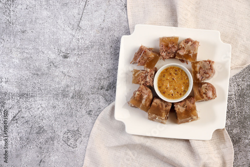 Aspic or jellied meat on a plate with mustard on a dark grey background. Top view, flat lay