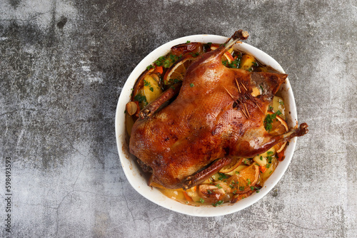 Roast duck with oranges, potatoes and herbs in a white baking dish on a dark grey background. Top view, flat lay