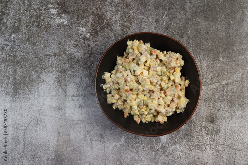 Homemade Russian salad or Olivier from boiled vegetables and sausage in a bowl on a dark background. Top view, flat lay  .