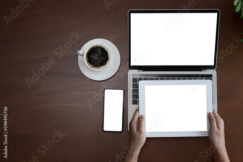 Vintage wooden hipster desktop top view cup of coffee, woman hands using laptop, smartphone and holding tablet screen