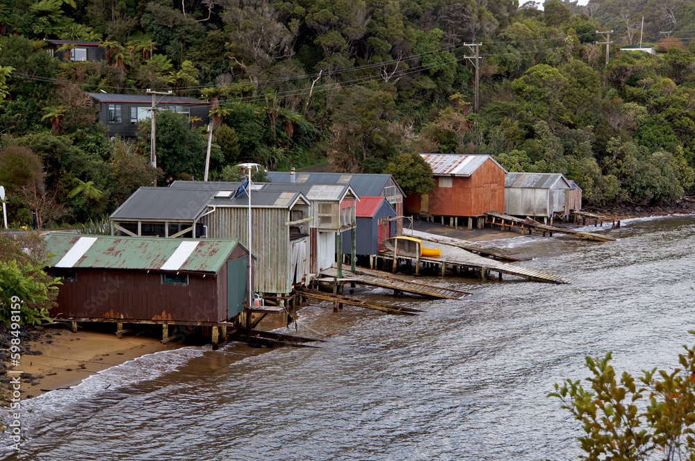 Colourful row of boathouses and boat ramps in a sheltered bay surrounded by bush-covered hills, Stewart Island, New Zealand.