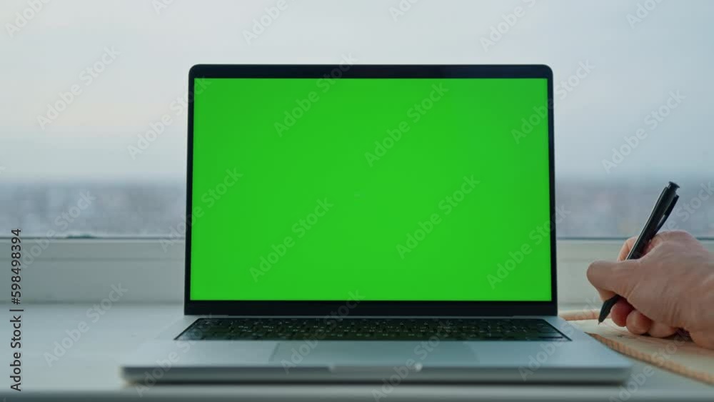 man writing in notebook near laptop with green screen workplace with big window at home or office Generative AI man writing in notebook near laptop with green screen workplace with big window at home or office Generative AI