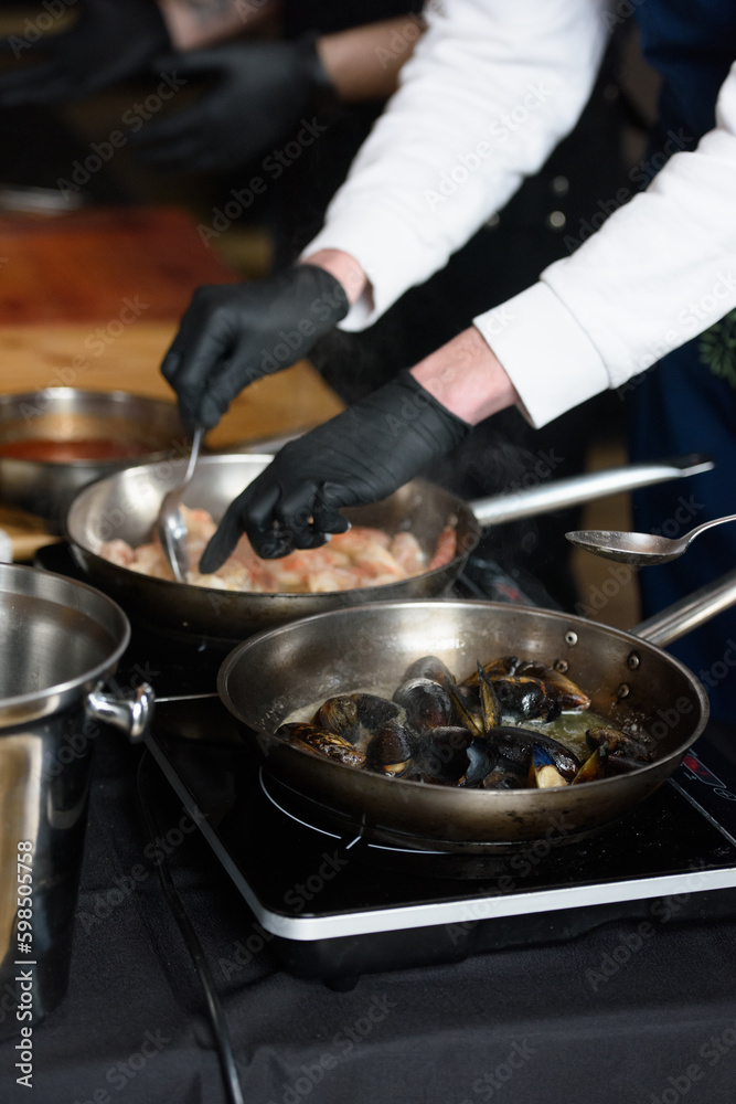 the chef in the restaurant is frying mussels in a steel pan the chef in the restaurant is frying mussels in a steel pan
