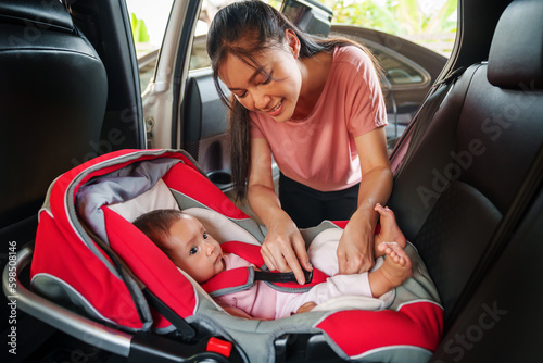 Obraz na płótnie happy mother is fastening safety belt to newborn baby in car seat