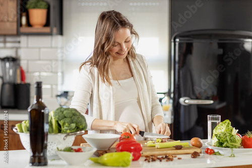Pregnant woman prepare vegeterian meal in the kitchen with knife in hand