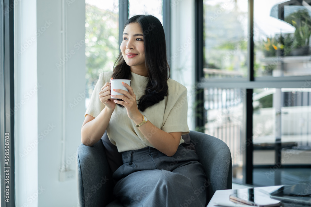 Asian businesswoman smiling happily with a new morning holding a cup of coffee lightly sipping coffee professional woman in size working in the office