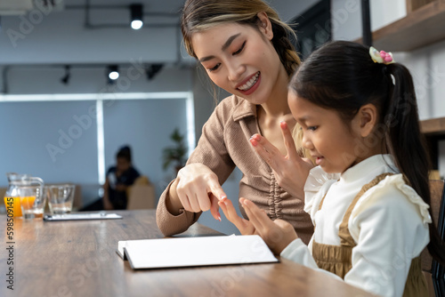 Beautiful mother teaching her lovely daughter to do homework in living room