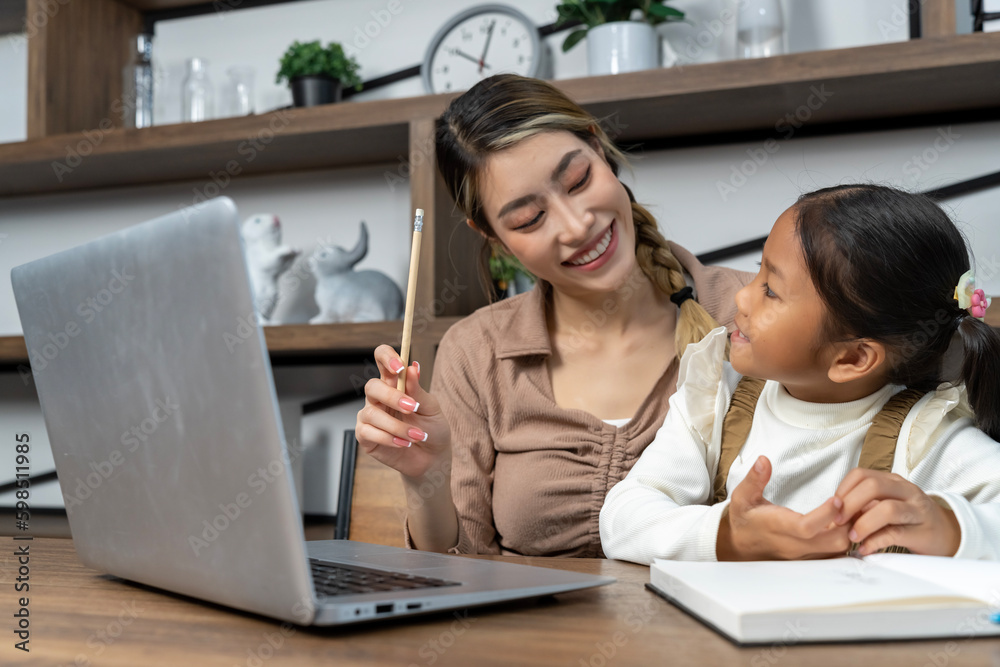 Beautiful mother teaching her lovely daughter to do homework in living room Beautiful mother teaching her lovely daughter to do homework in living room