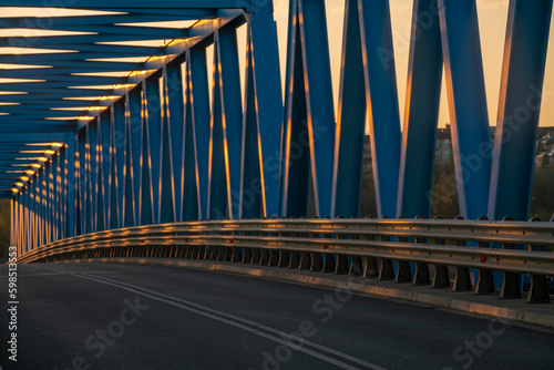 Asphalt road running over a truss bridge at sunset
