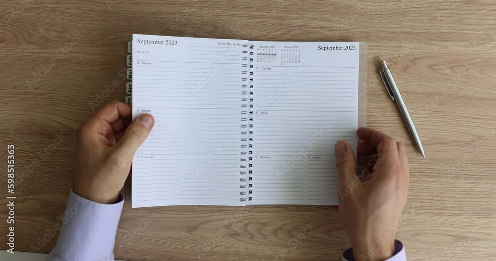 Man hands flip through paper planner lying on wooden table near silver ballpoint pen. Employee in office shirt chooses day to write meeting date