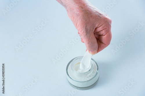 Elderly woman's hand taking cosmetic product from jar, advertisement of hand cream for retired to stop aging process