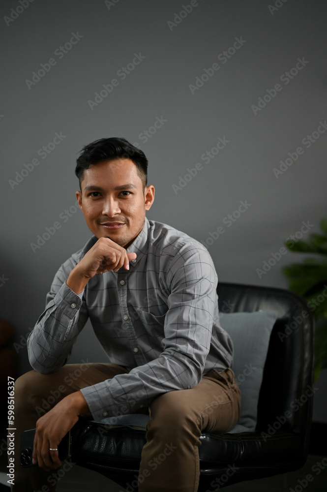 Portrait of a handsome millennial Asian man in casual clothes sits on a black leather chair Portrait of a handsome millennial Asian man in casual clothes sits on a black leather chair
