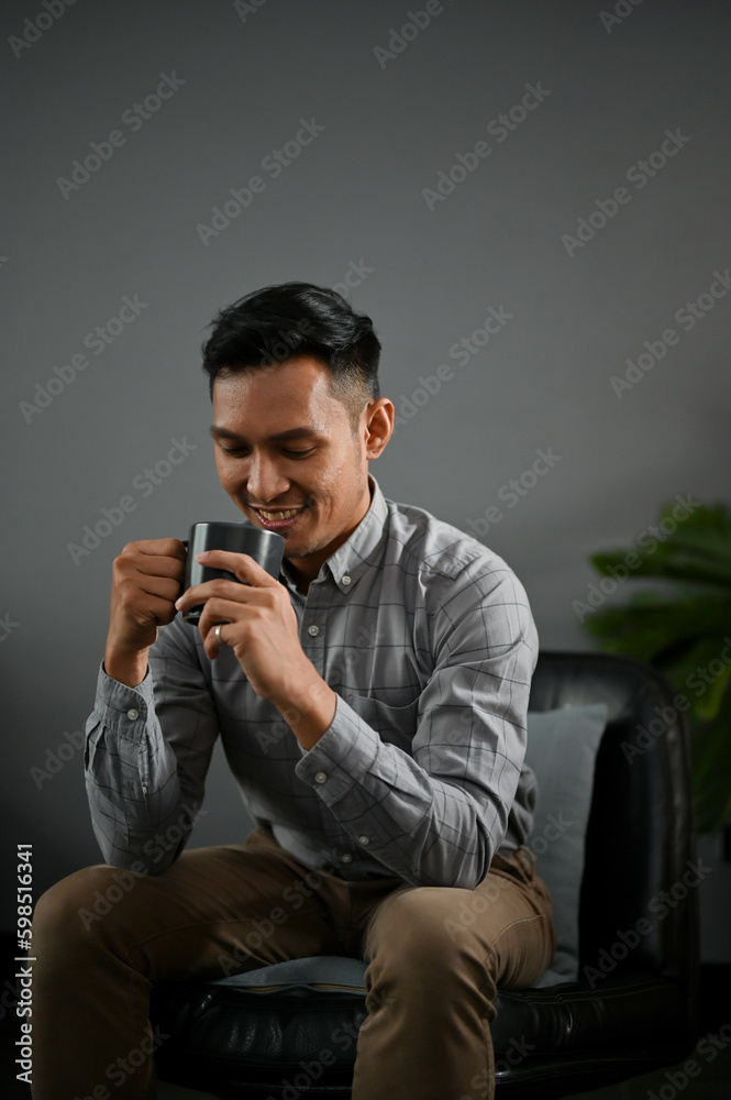 A happy and relaxed adult Asian man enjoying with his morning coffee in his living room. A happy and relaxed adult Asian man enjoying with his morning coffee in his living room.