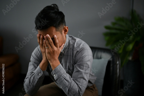Stressed and depressed Asian man is covering his face, crying about his failures in life