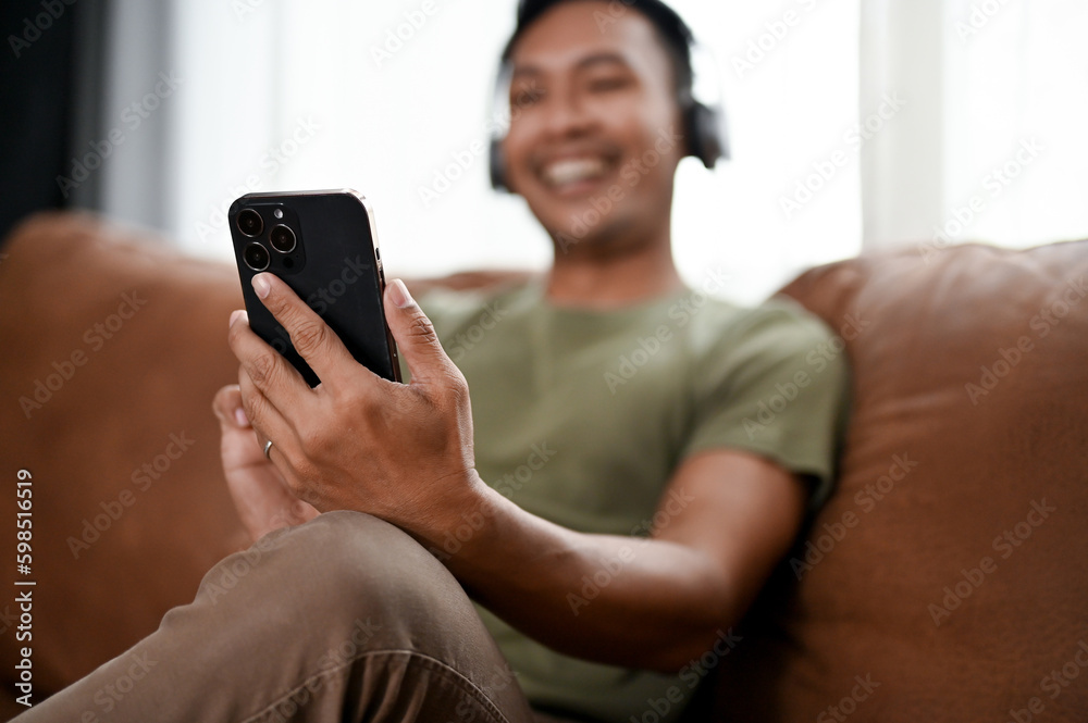 Happy Asian man using his smartphone and relaxing on a sofa in his living room. Happy Asian man using his smartphone and relaxing on a sofa in his living room.