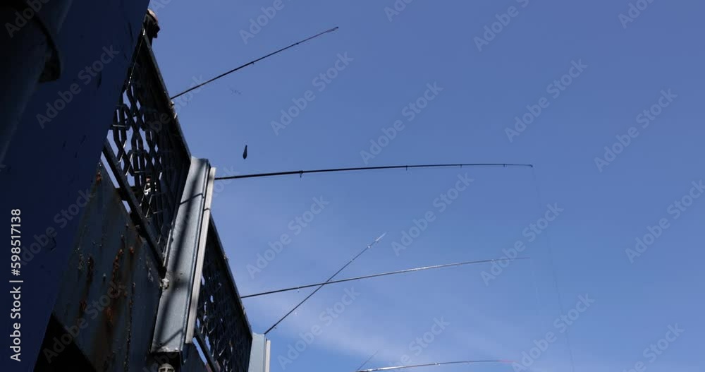 Fishermen catch fish standing on bridge over river. Fishing rods under blue summer sky. Active recreation and hobby low angle shot slow motion