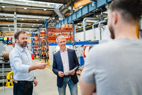 Smiling manager with businessman discussing with employee at factory photo
