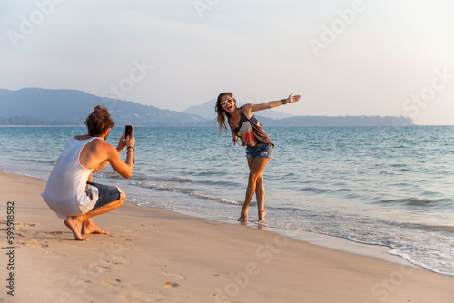Man photographing girlfriend enjoying near shore at beach photo