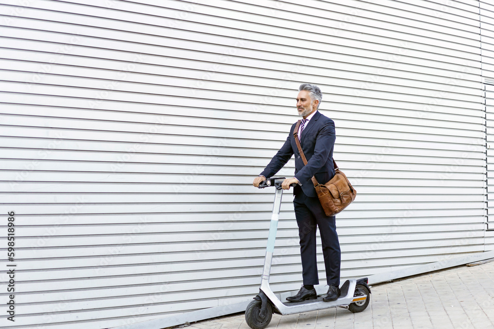 Businessman riding electric scooter near wall Businessman riding electric scooter near wall