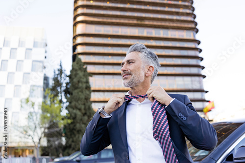 Mature businessman removing tie in front of building