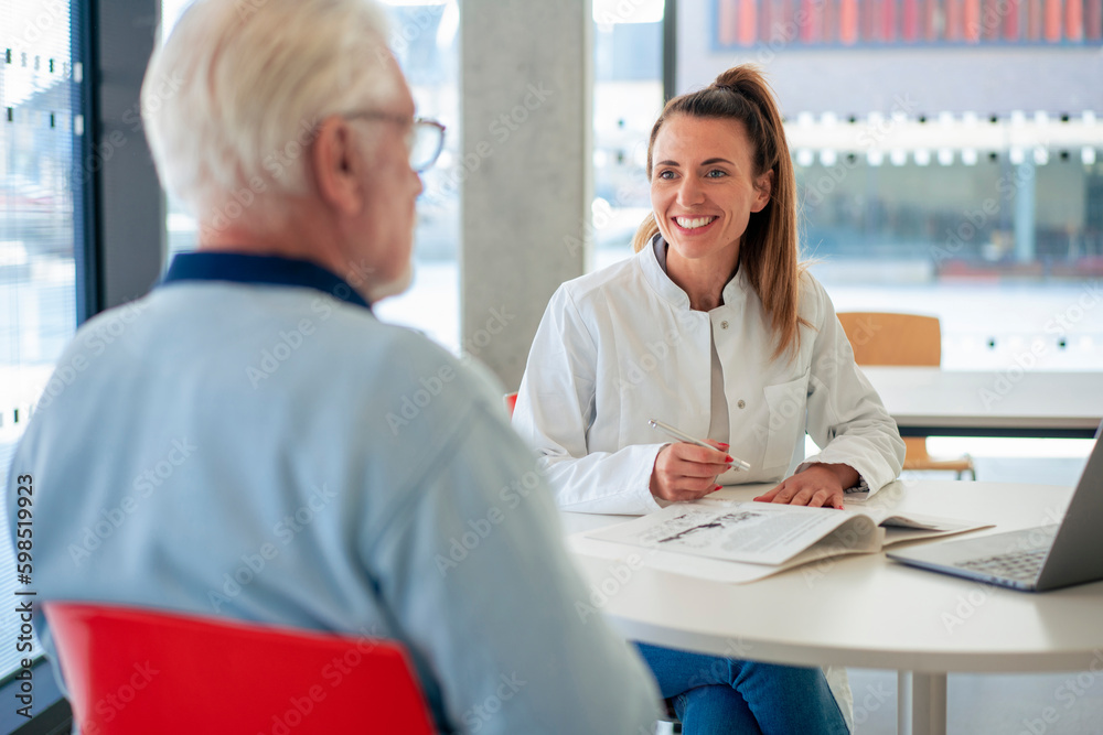 Happy doctor with file discussing with patient sitting at clinic Happy doctor with file discussing with patient sitting at clinic