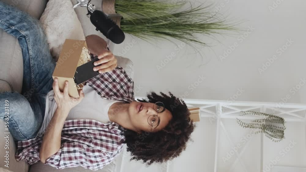 Vertical video. Phone unboxing. Tech vlog. Electronics review. Cheerful blogger guy unpacking gadget recording content speaking into microphone in modern home studio interior. Generative AI