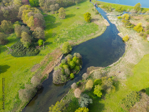 Drone view of a fresh water river seen entry from a large lake. A small natural river Island is seen. In the area of rare white deer which can be seen grazing below. © Nick Beer