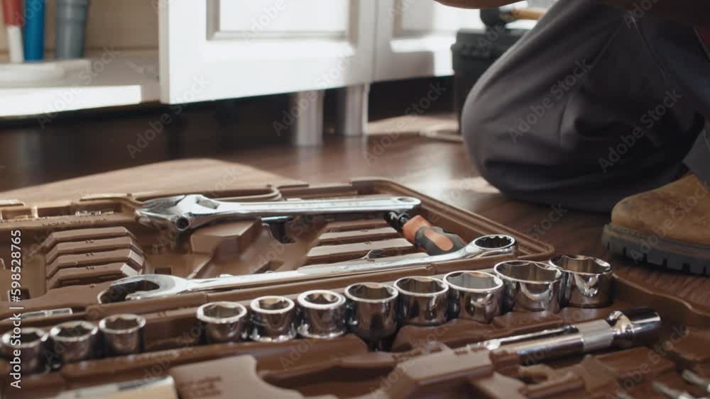 Close-up shot of unrecognizable Black plumber sitting on floor choosing tools to repair sink drain
