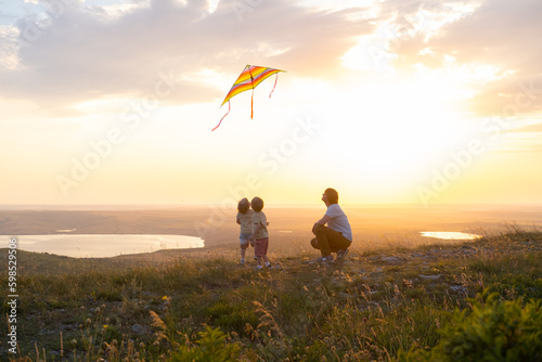 Happy man and children  father and sons  with kite in nature at sunset