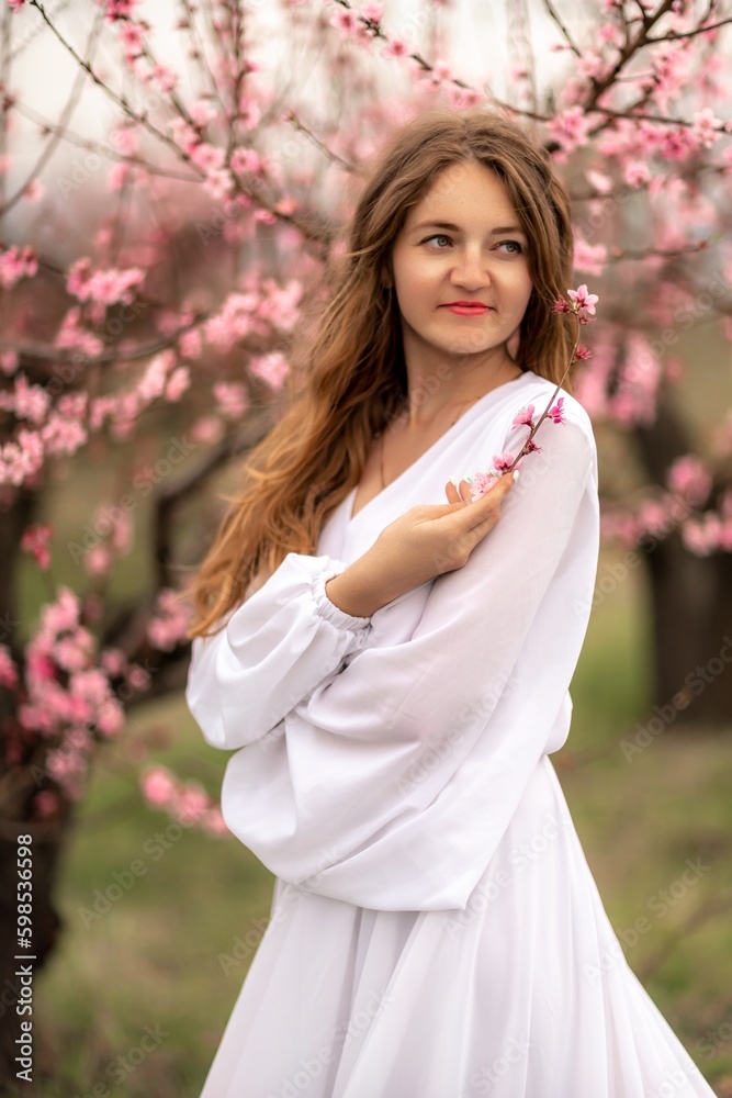 Woman peach blossom. Happy curly woman in white dress walking in the garden of blossoming peach trees in spring