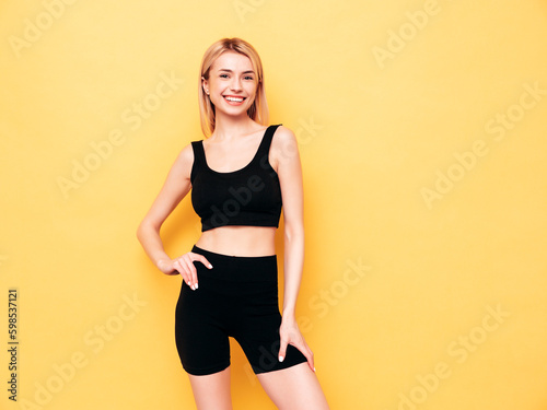 Young beautiful smiling blond female in summer cycling shorts clothes. Sexy carefree woman posing near yellow wall in studio. Positive model having fun indoors. Cheerful and happy