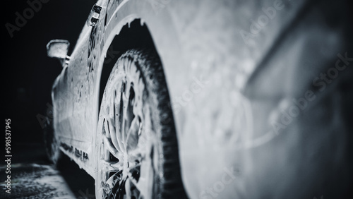 Aesthetic Photo of a Black Family SUV Covered in Washing Soap and Foam. Close Up Shot of Foam Dripping from Car s Rear Wheel Arch onto the Electric Car s Tyre and Rim